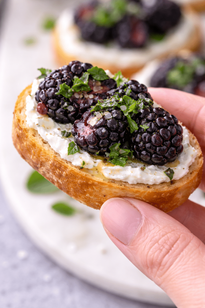 woman holding the blackberry goat cheese mint crostini