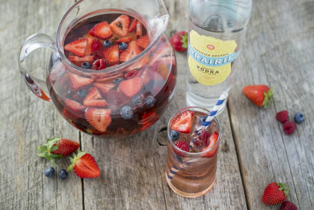 Pitcher of berry sangria with strawberries and blueberries beside a bottle of Prairie Organic Vodka
