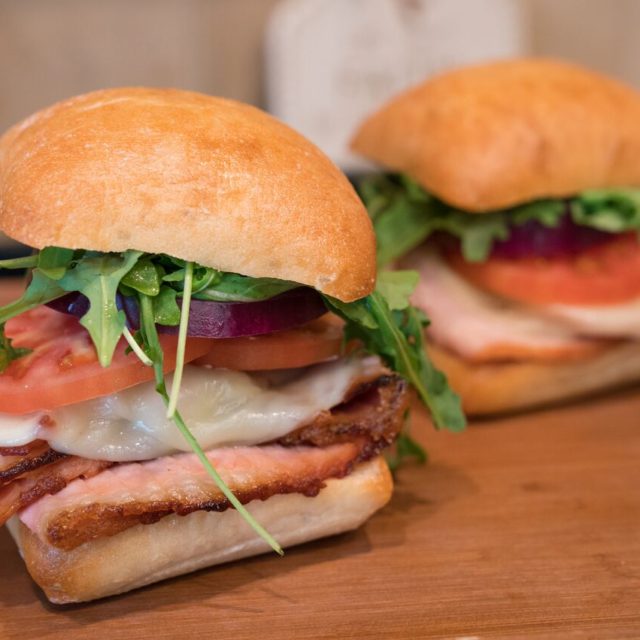 Hot ham and provolone sandwich with bacon, tomato, red onion and arugula on a ciabatta roll