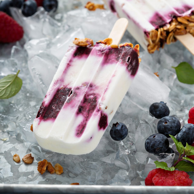 Yogurt parfait breakfast popsicles with berry jam swirls and granola on a tray of ice with fresh berries