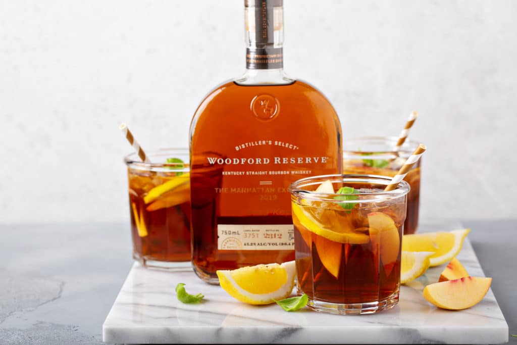 Bourbon peach tea smash cocktails beside a bottle of bourbon