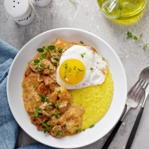 Overhead view of shrimp and grits topped with a fried egg in a white bowl with a blue napkin and olive oil