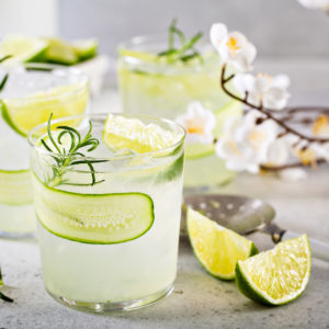 Cucumber rosemary gin cocktails over ice with lime wedges and white blossoms