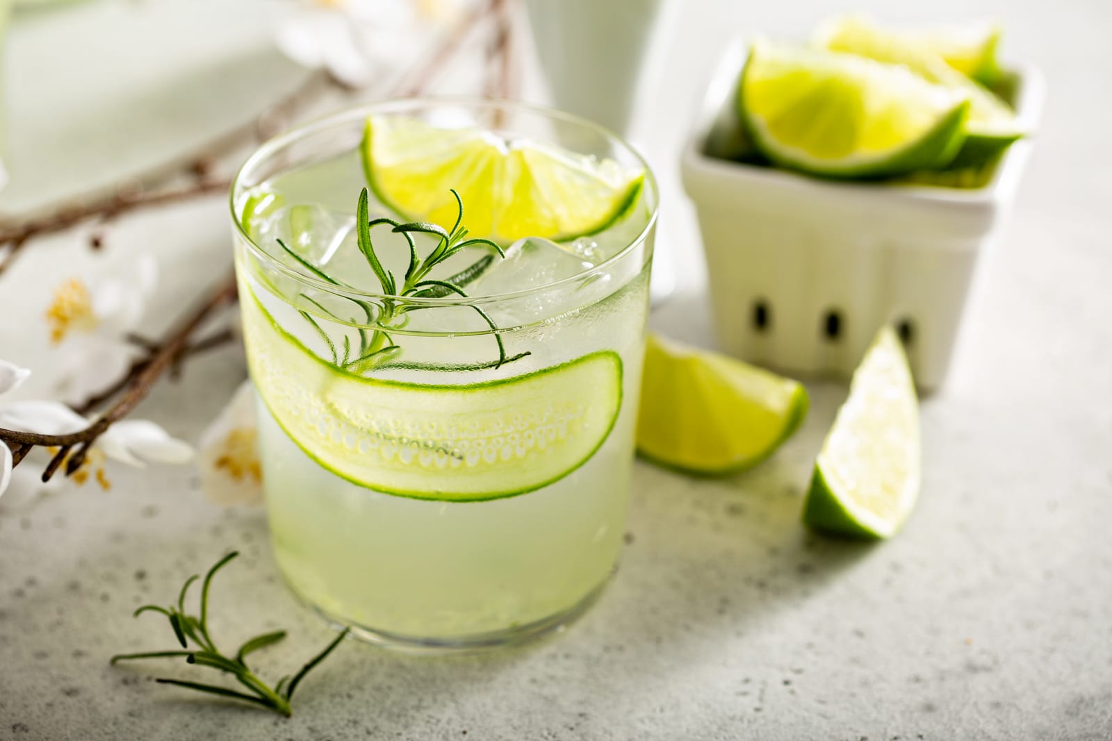 Cucumber gin gimlet with cucumber ribbon, lime and rosemary beside a basket of lime wedges