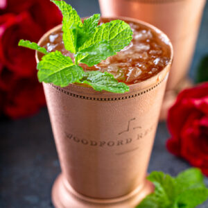 Mint julep in a copper julep cup with fresh mint and red roses
