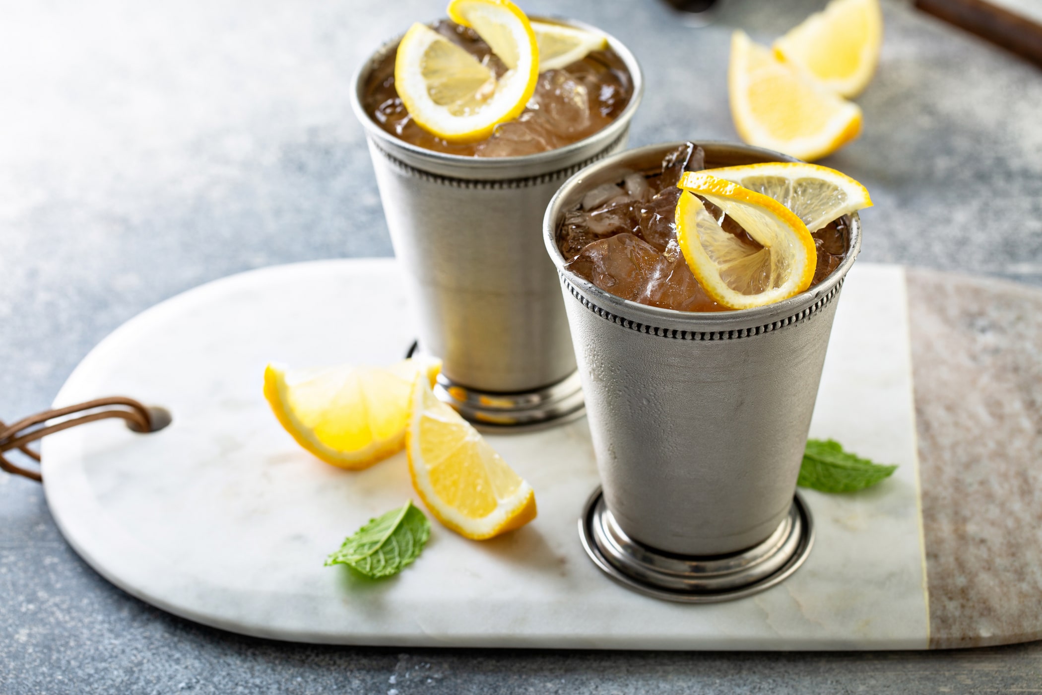 Two silver julep cups with lemon twists and mint on a marble board
