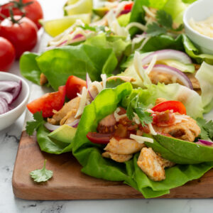Close-up of chicken lettuce wraps filled with seasoned chicken, tomato, cheese, red onion and avocado on a wood board