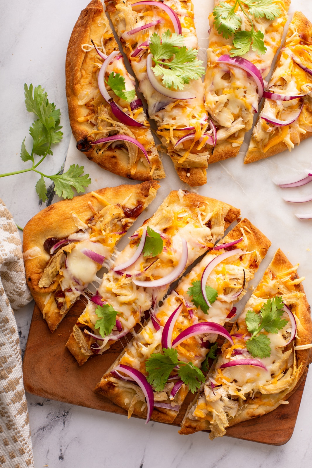 Sliced BBQ chicken flatbreads on a wooden board garnished with red onion and cilantro
