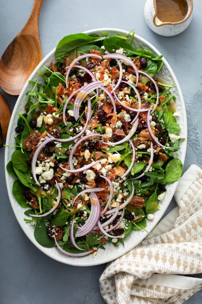 Cranberry pecan salad on a white oval platter with a linen napkin and a small jug of apple vinaigrette