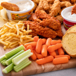 Fried chicken board with a tender dipped in Heluva Good dip, fries, carrots, celery and garlic toast
