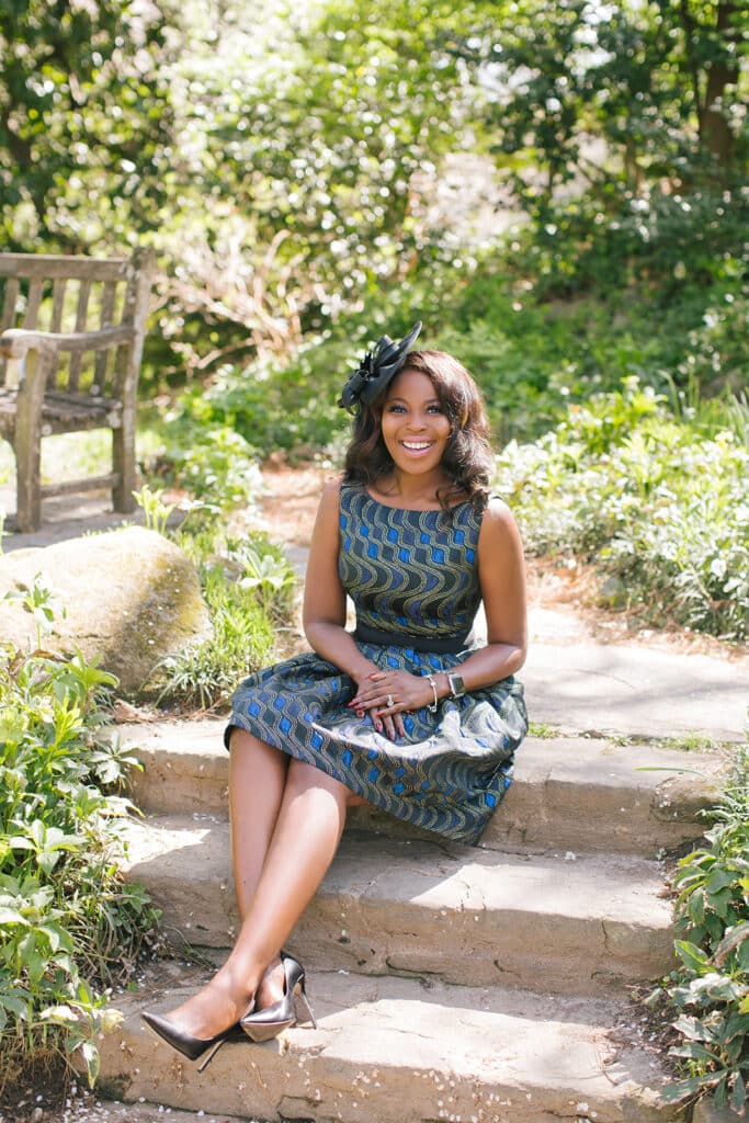 Erica Thomas seated on stone garden steps in her Kentucky Derby fascinator and print dress