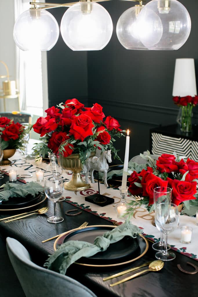 Kentucky Derby table set with red rose centerpieces, white taper candles and sage napkins under glass globe pendants
