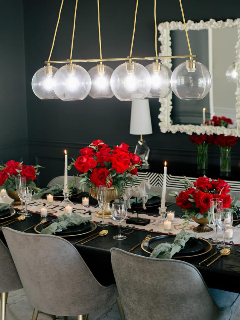 Full Kentucky Derby dinner table with red rose centerpieces, white tapers and gray velvet chairs beneath glass globe pendants