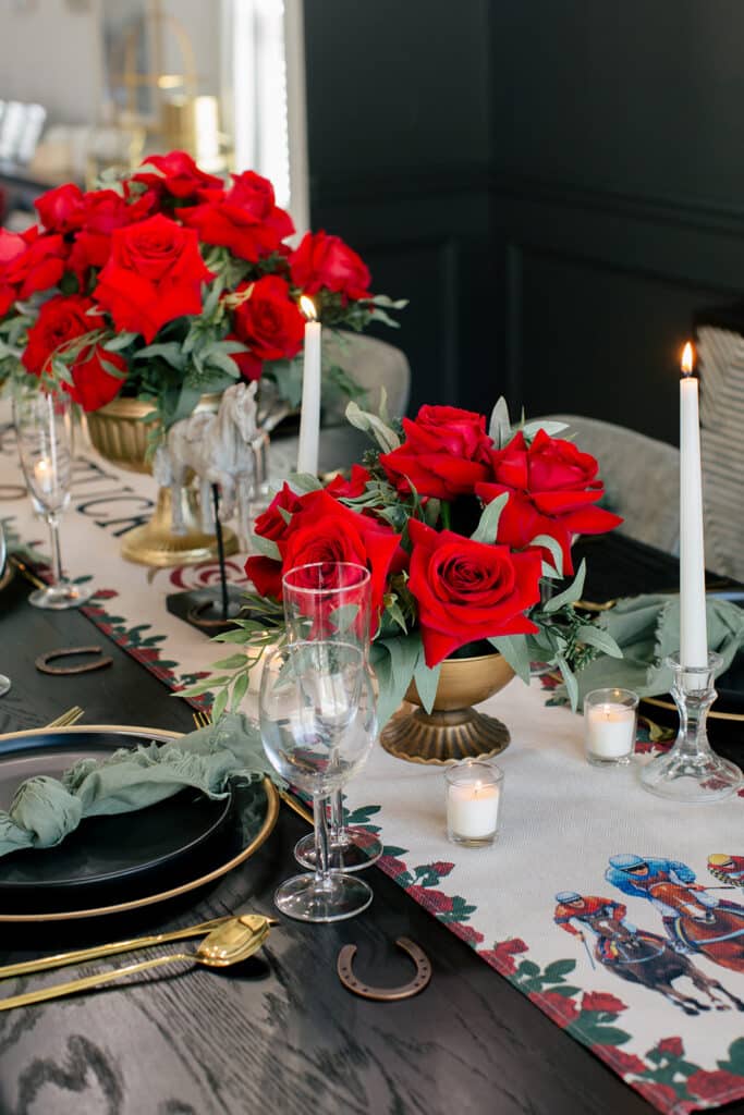 Red roses in gold urns, white tapers in crystal holders and glowing votives along a table runner printed with racing horses and jockeys