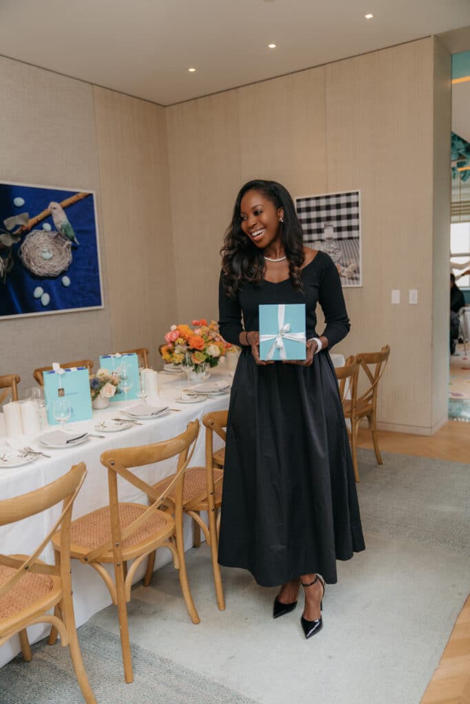 Erica A. Thomas holding a gift bag beside the Friendsgiving table at The Blue Box Café