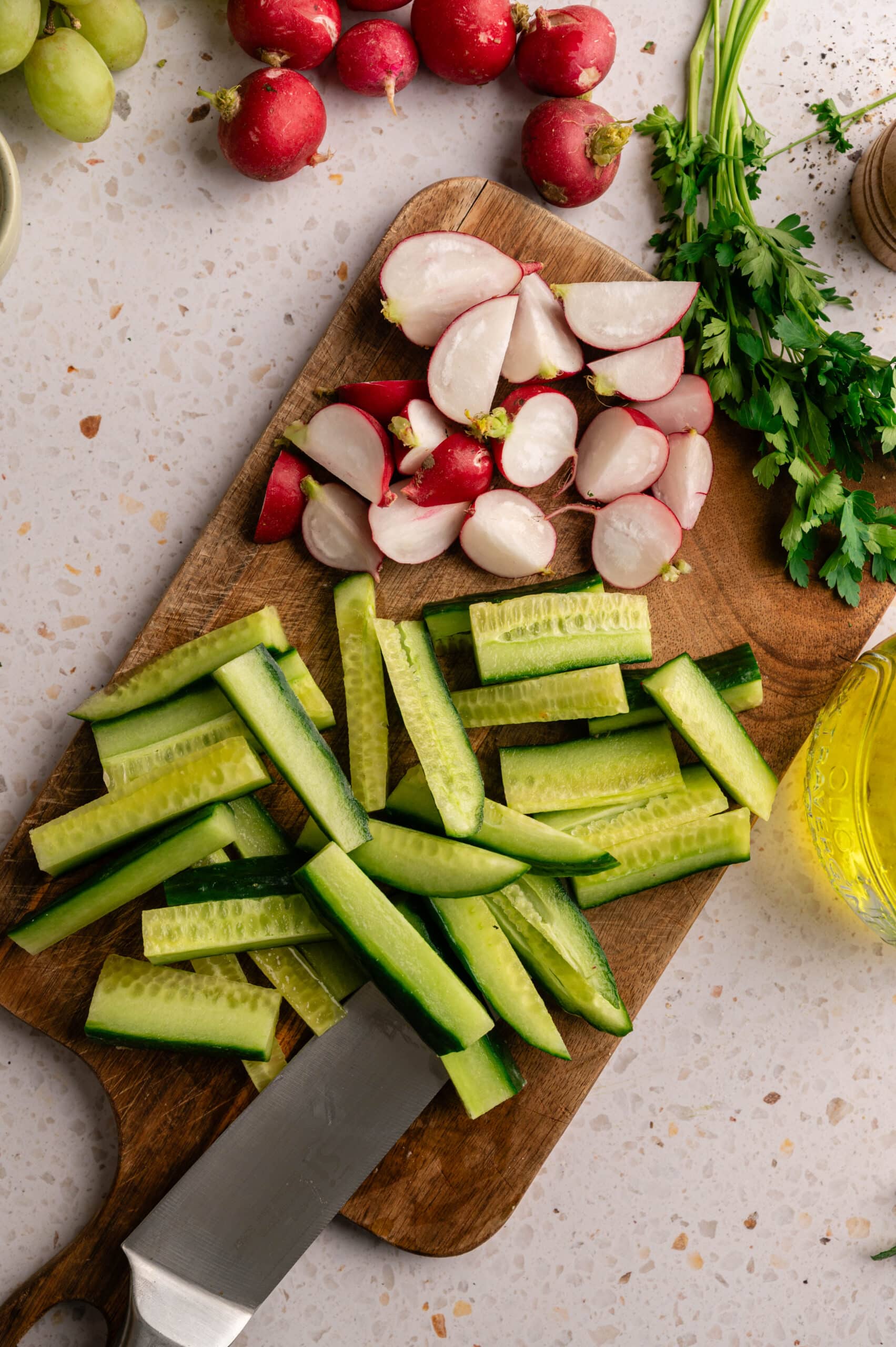 Sliced cucumber and radishes on a wooden board with a knife