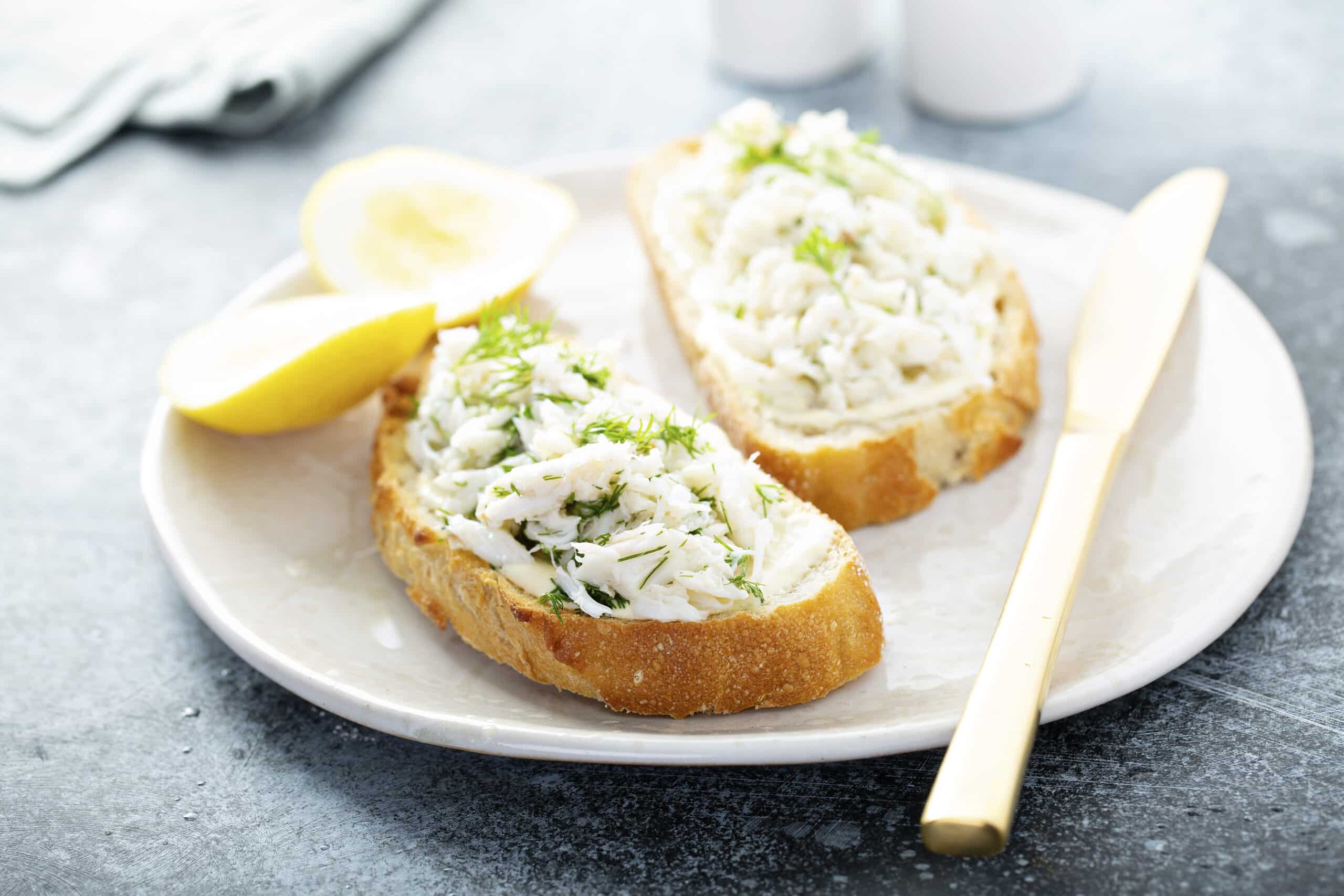 Crab meat and dill toast with lemon in white plate