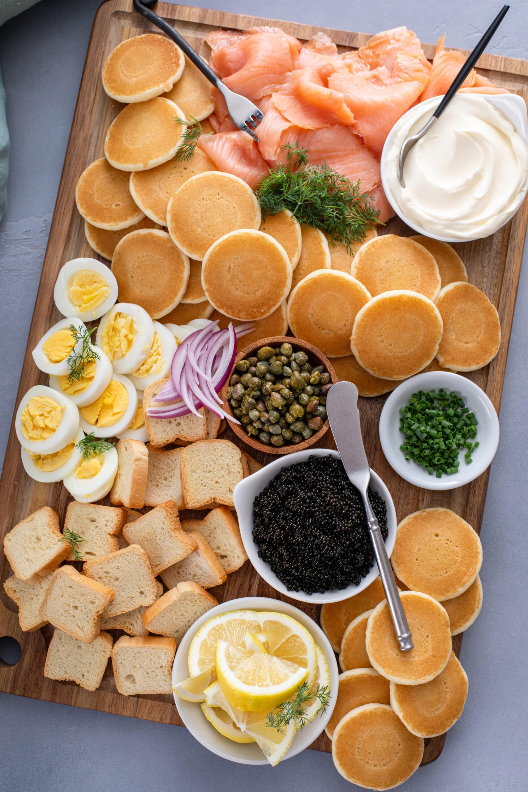 Blini, halved hard-boiled eggs, red onion, capers and black caviar on a wooden serving board