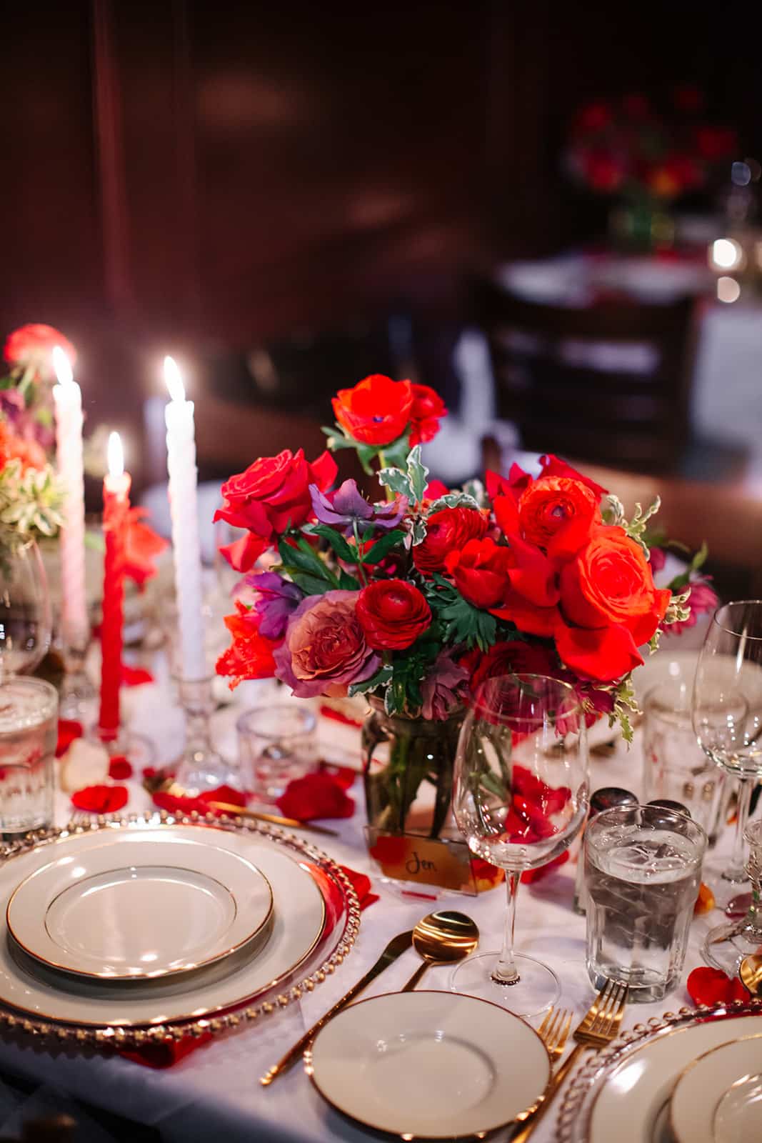Close-up of a handwritten place card, red rose centerpiece, and taper candles on the table