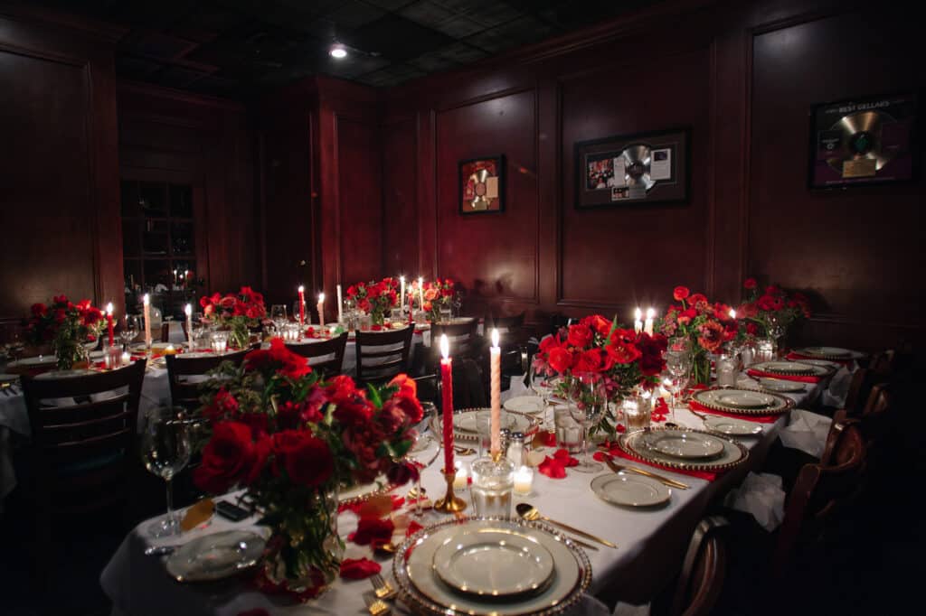 Wide view of the wood-paneled dining room set for Galentine's dinner with rose-lined tables and taper candles