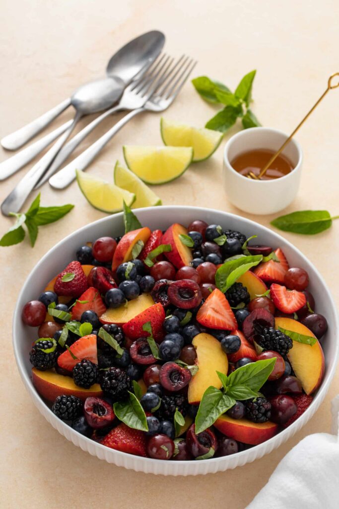 Honey Basil Peach Fruit Salad with utensils, drizzle and lime
