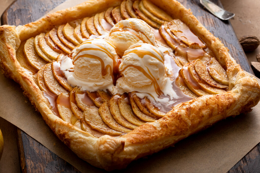 Square apple galette topped with vanilla ice cream and caramel drizzle on a wooden board