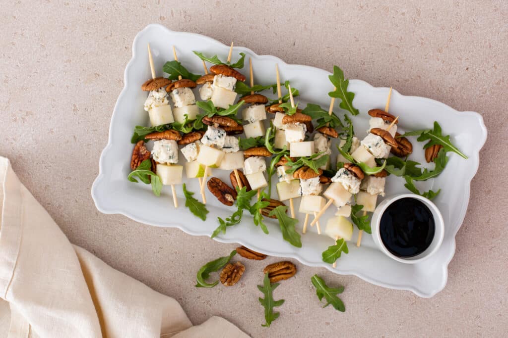 Pear and Bleu Cheese Appetizer Skewers with Arugula and Pecans on a serving platter with balsamic glaze