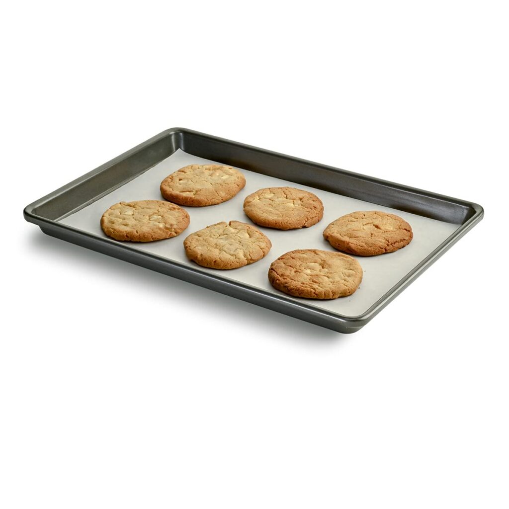 Metal baking sheet pan with baked cookies on parchment paper
