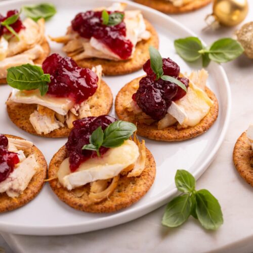 Close-up of turkey, brie and cranberry sauce crackers garnished with basil on a white plate with gold ornaments