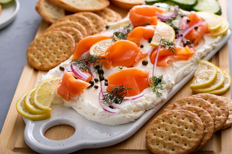 Smoked salmon charcuterie board with cream cheese, capers, and fresh dill on a wood board