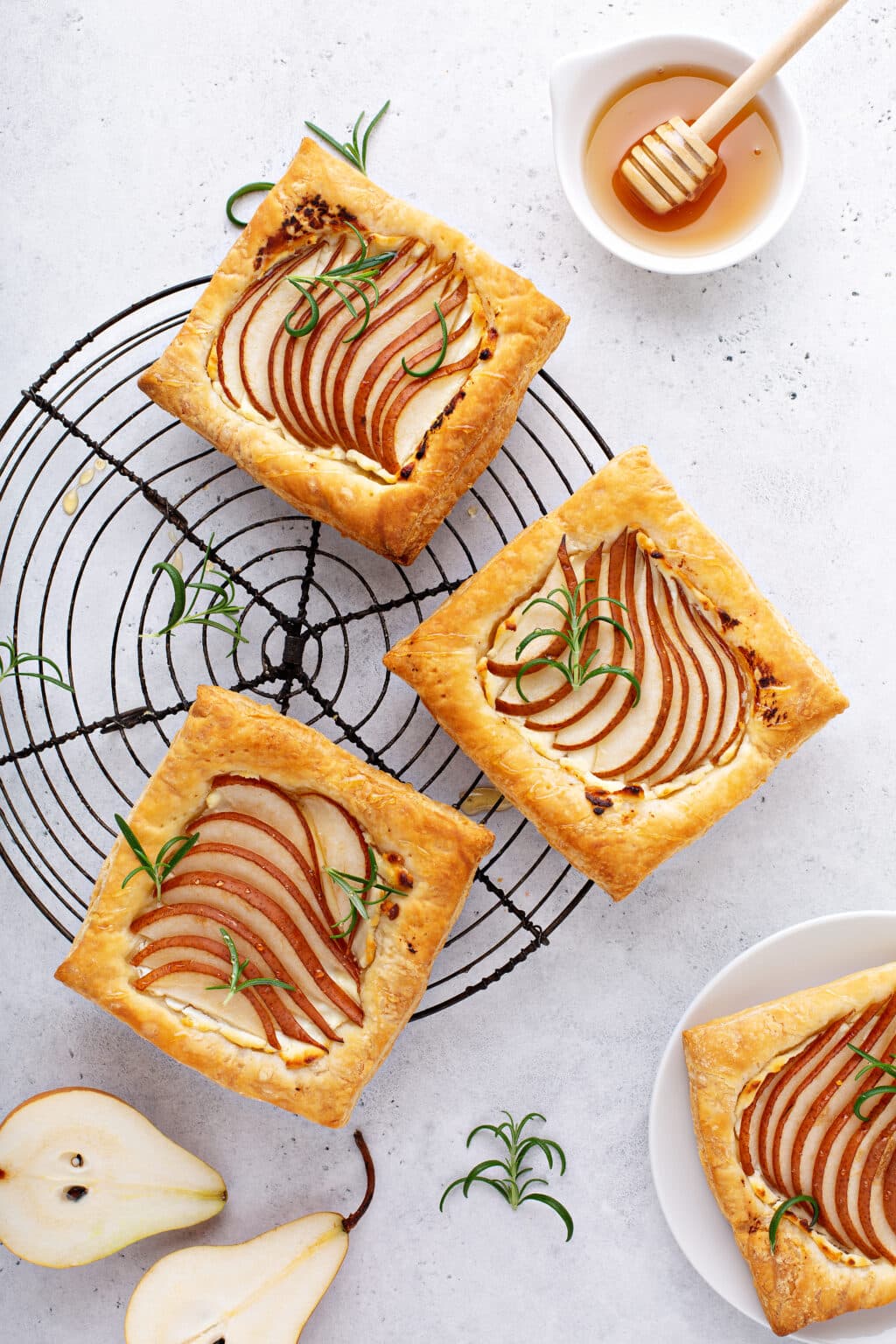 Pear puff pastry tarts topped with goat cheese, rosemary, and honey on a cooling rack