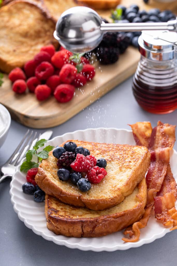 One serving of Easy French Toast Board with syrup, fruits, bacon sprinkled with powdered sugar