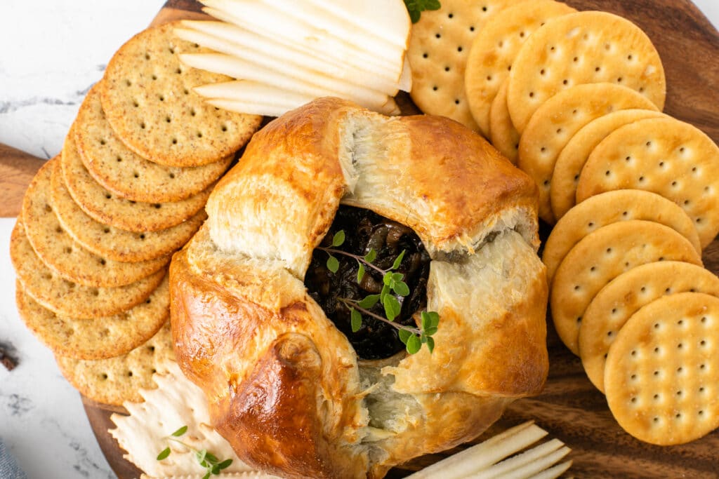 Baked Brie With Balsamic Caramelized Onions served with crackers and fruit slices, close up shot