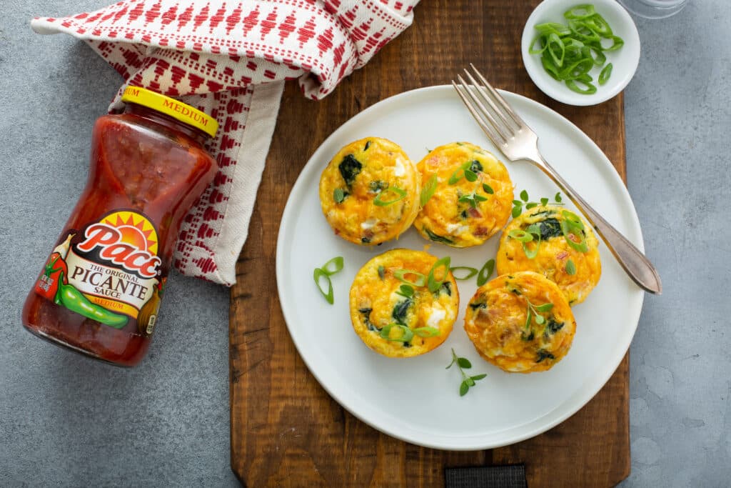 Served in white platter the Bacon Spinach & Cheese Egg Muffins with Pace picante sauce on the picture