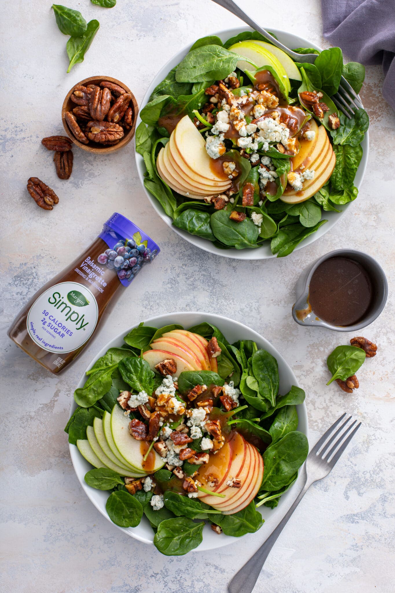 2 servings of The Perfect Winter Salad served with the store bought dressing, with the pair of wooden spoon and pecans on the side