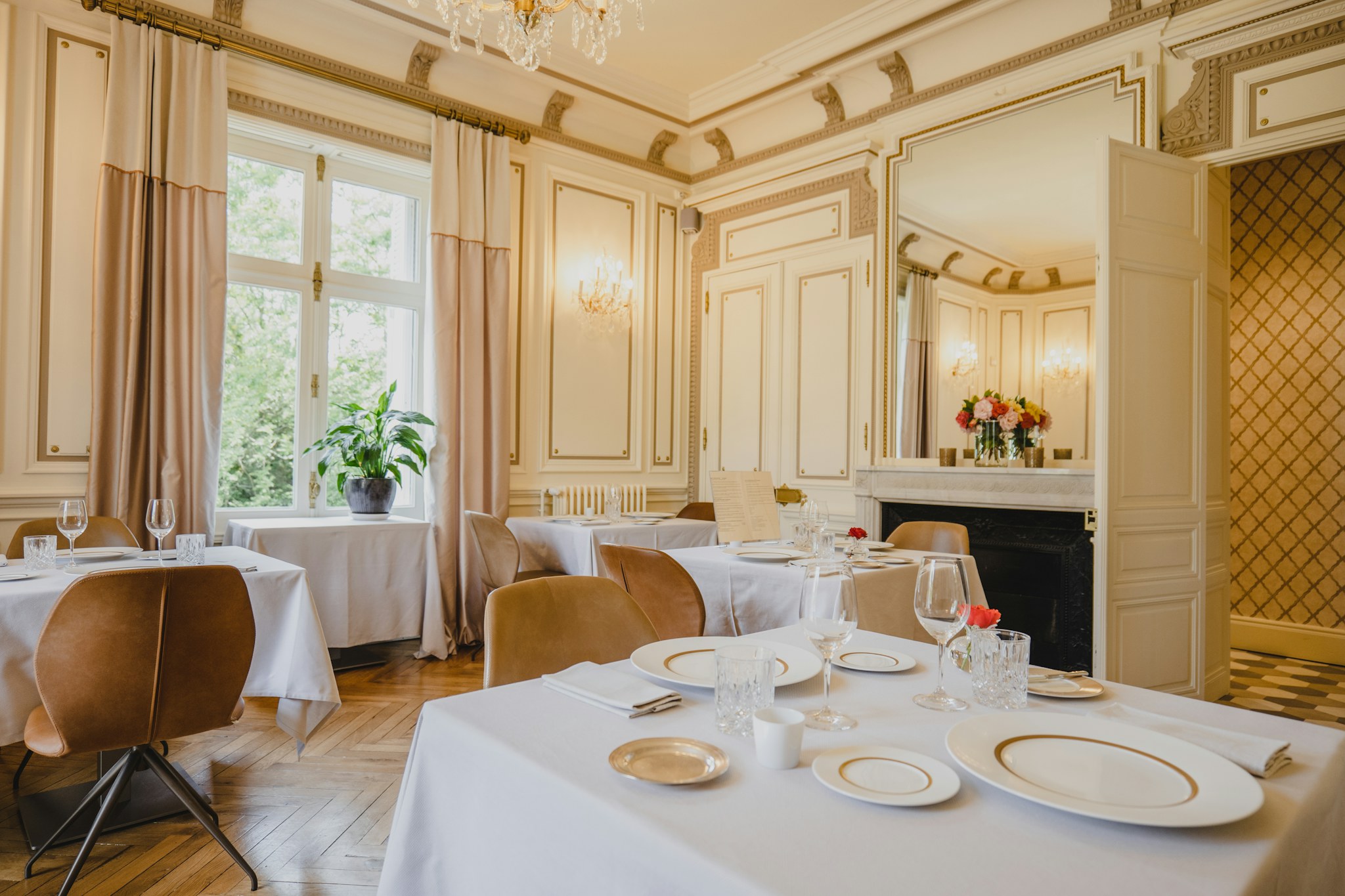 Restaurant dining room with white tablecloth tables set for service beside tall windows