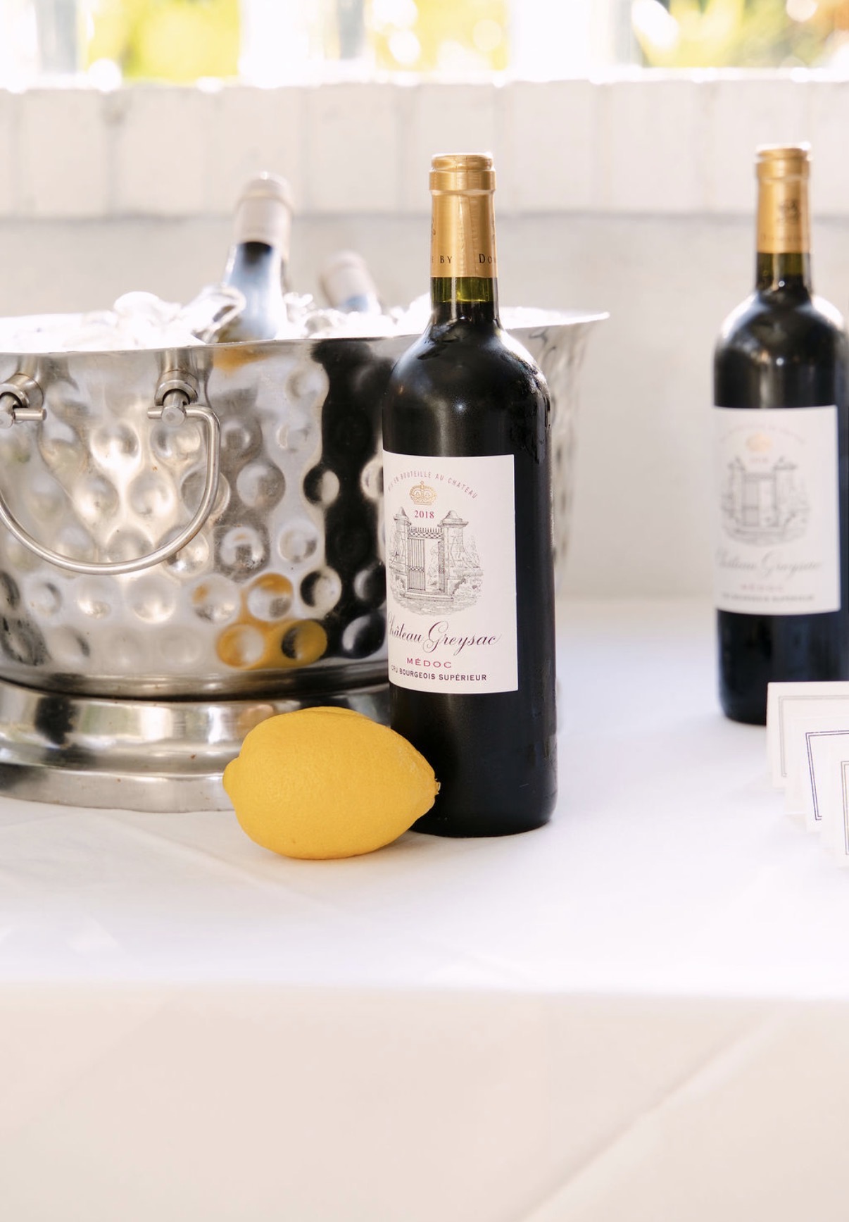 Bottles of Château Greysac 2018 Médoc beside a lemon and a hammered silver ice bucket