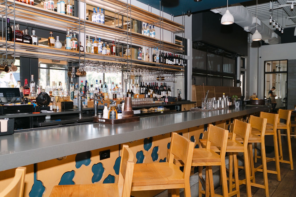 The bar at Foundation Social Eatery in downtown Alpharetta, lined with wooden stools and backlit shelves of spirits