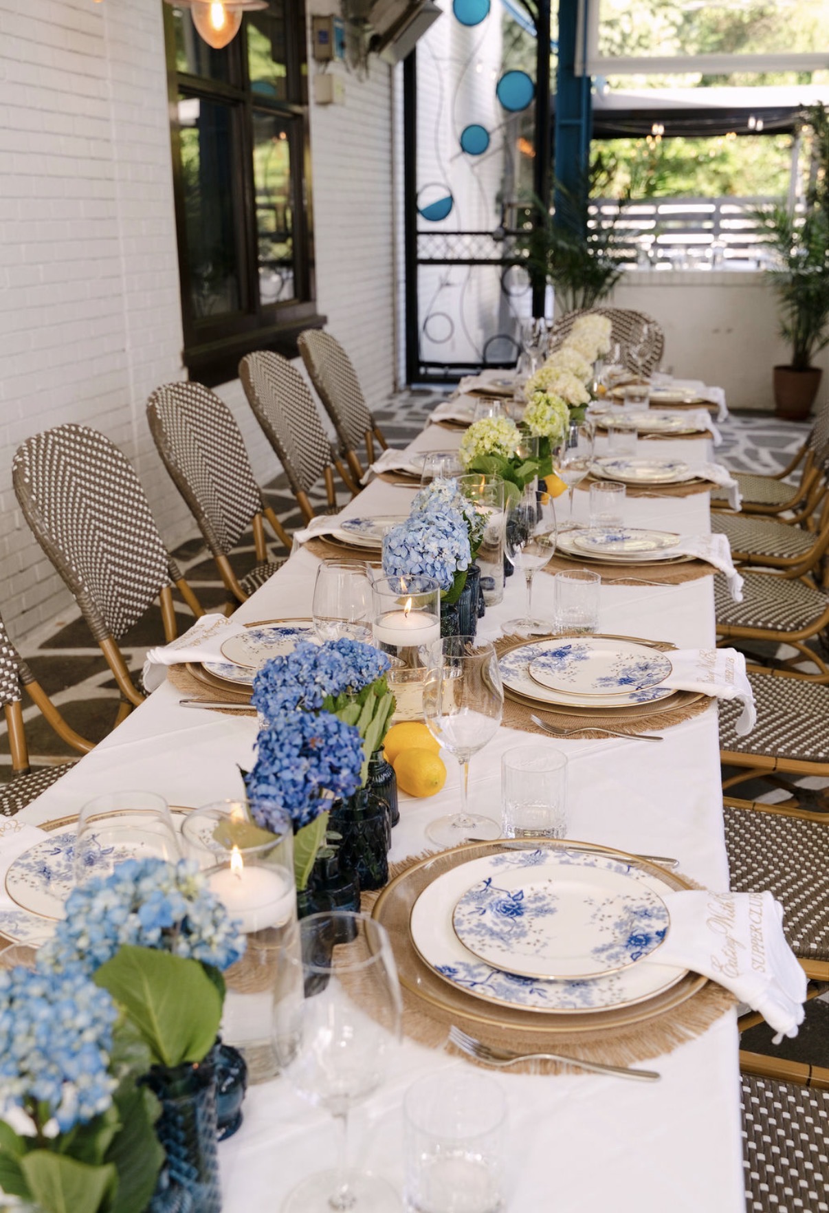 Long Greek-inspired dinner party table with hydrangeas moving from blue to white, floating candles, lemons and gold-rim chargers