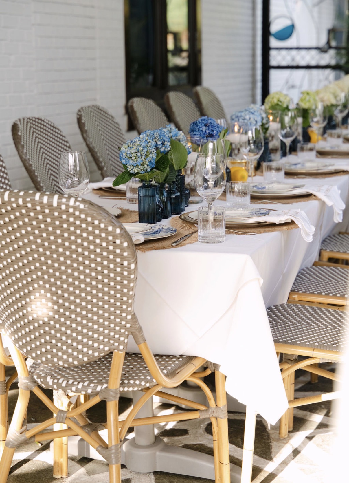 Blue hydrangeas in blue bud vases and a Lenox place setting beside a woven bistro chair
