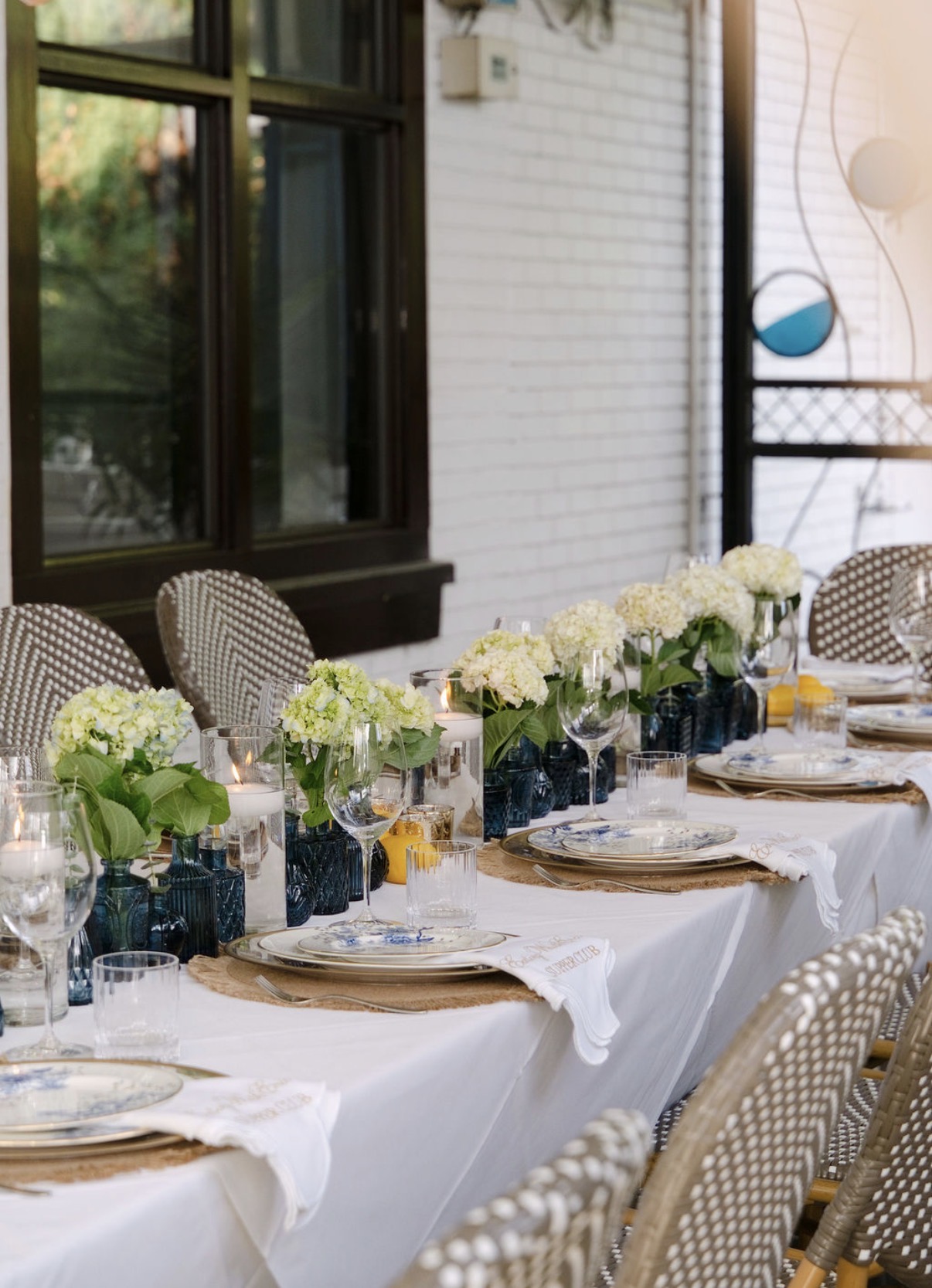 White hydrangeas in blue glass vases with floating candles, lemons and embroidered napkins down a long dinner table