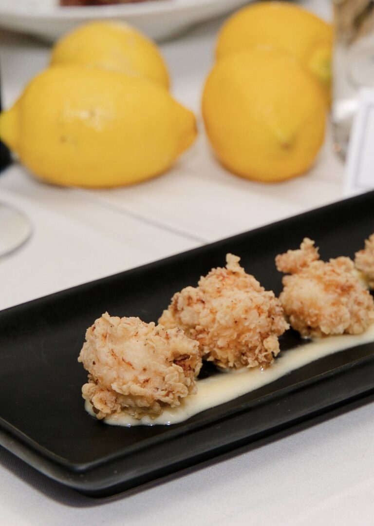 Papou Pano's lobster morsels at Kyma, lightly crisped and served over a creamy sauce on a black plate, with lemons behind
