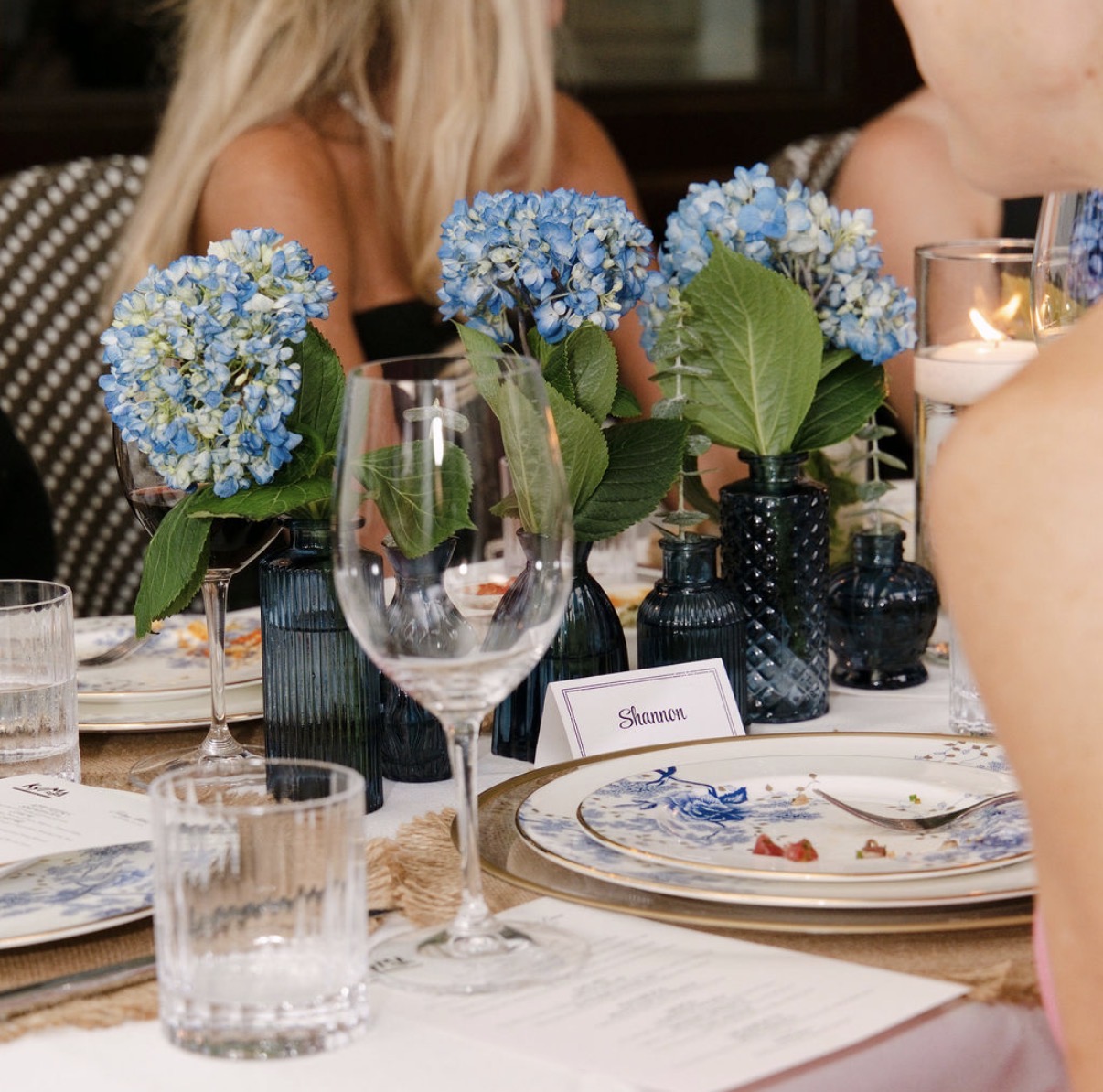 Blue hydrangeas in petite blue glass bud vases beside a place card at the Supper Club dinner at Kyma
