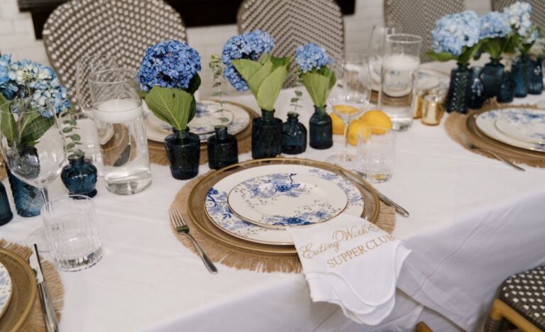 A place setting with Lenox Garden Grove china, a gold-rim charger, an embroidered napkin, lemons and blue hydrangeas in bud vases