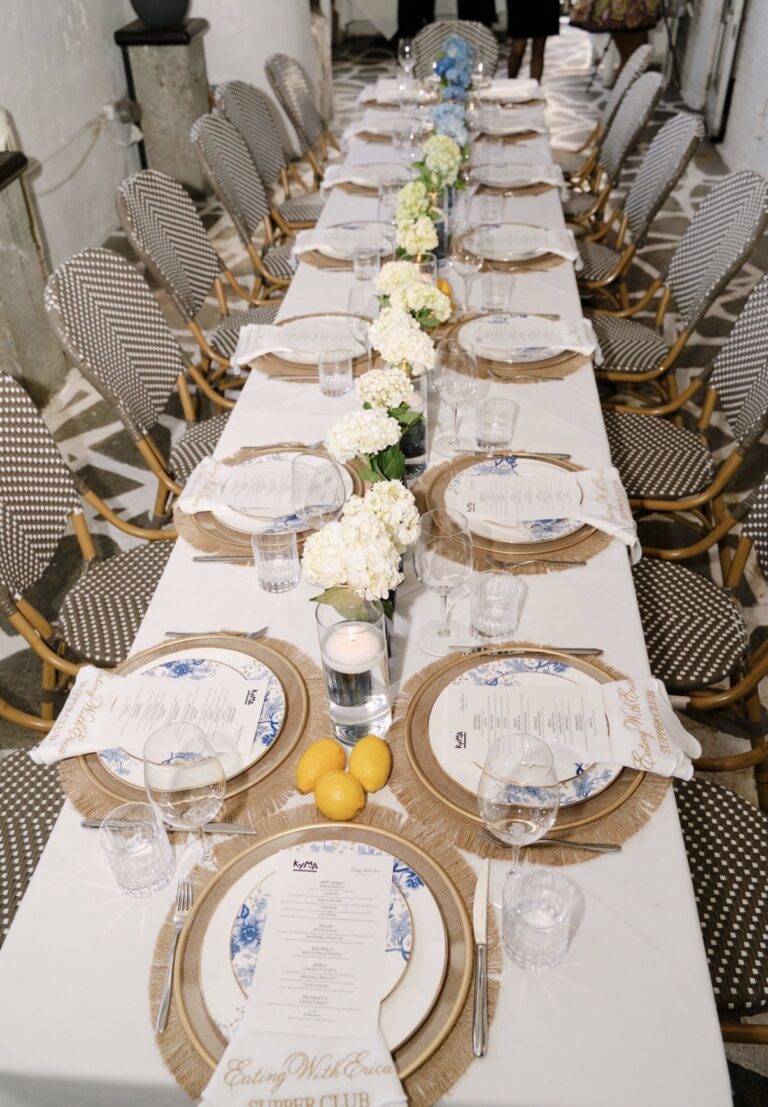 Overhead view of the Eating With Erica Supper Club table at Kyma with printed Kyma menus on blue floral plates, woven chargers, lemons and white hydrangeas