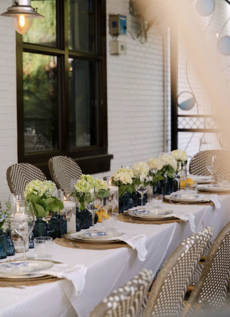 Supper Club table set against the white brick wall at Kyma in Buckhead, lined with white hydrangeas, blue glass vases and candlelight
