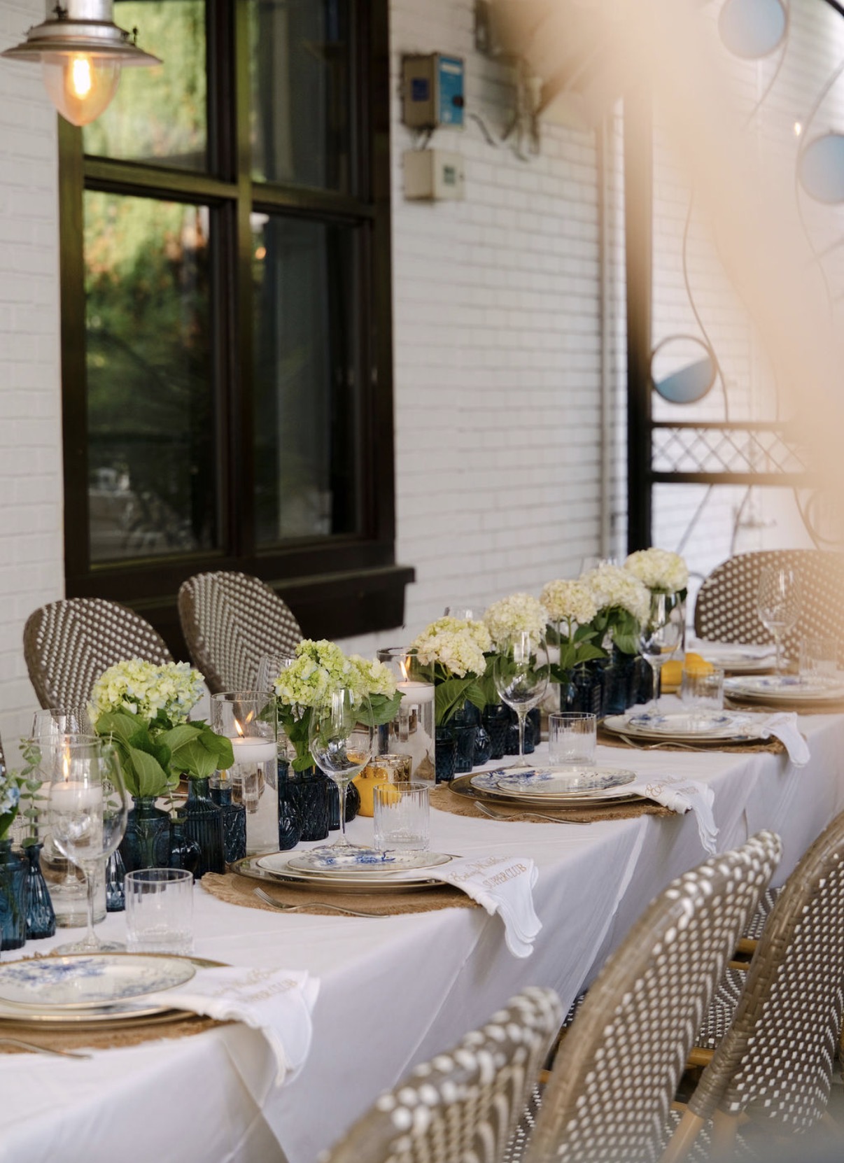 Supper Club table set against the white brick wall at Kyma in Buckhead, lined with white hydrangeas, blue glass vases and candlelight