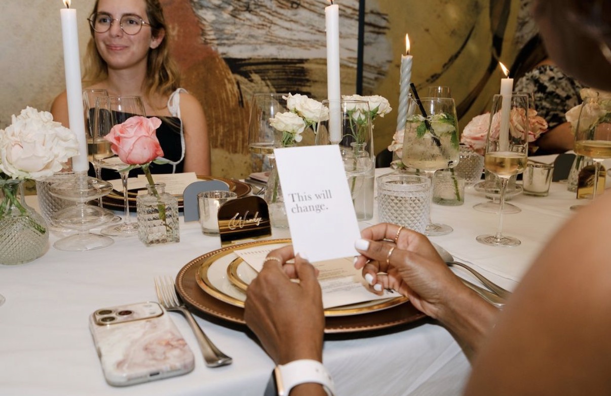 Supper Club guest holding a note reading “This will change.” pulled from beneath her charger at the Foundation Social Eatery table