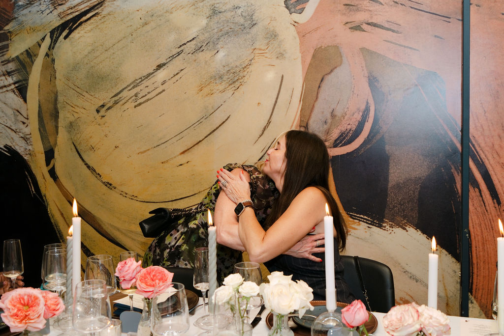 Two Supper Club guests embracing at the table in front of a painted mural at Foundation Social Eatery