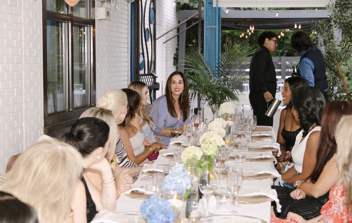 Eating With Erica Supper Club guests laughing and talking down the length of the table on the patio at Kyma